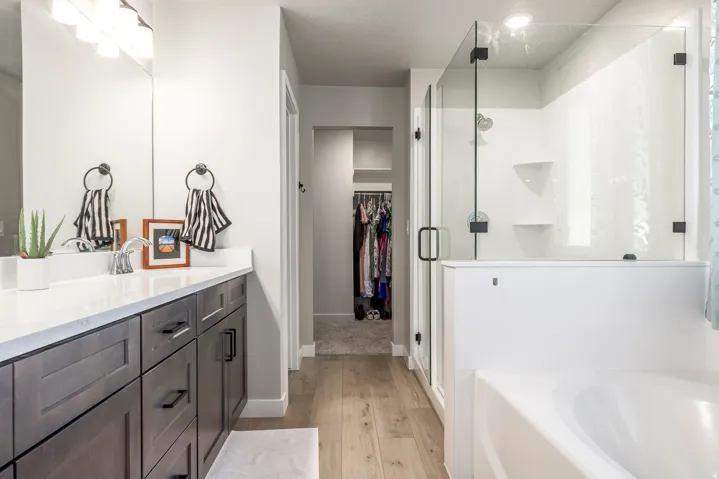 Dual-sink vanity with a light countertop, wood-finish flooring, glass-enclosed shower, and built-in bathtub
