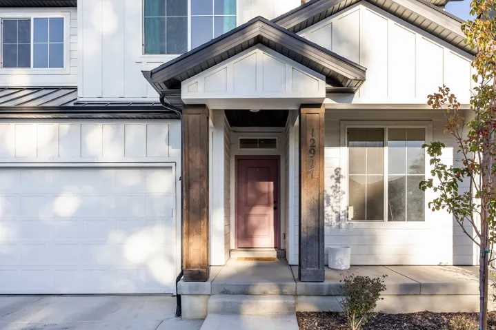 Board and batten siding, dark-framed windows, white panel garage door, covered entryway, and concrete porch