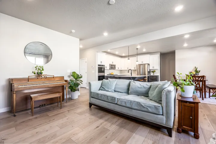 Expansive living area with wood-finish flooring, recessed lighting, and a kitchen featuring white cabinetry, stainless steel appliances, and a central island