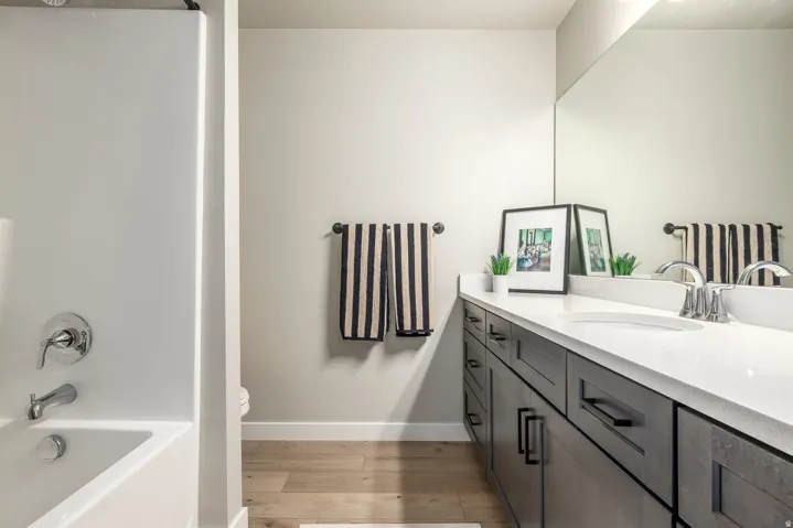 White built-in bathtub with chrome fixtures, wood-finish flooring, and a vanity with multiple drawers