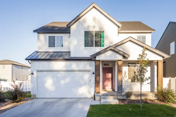 White exterior with vertical and horizontal siding, covered front porch with wood-finish posts, attached garage, and dark shingle roofing