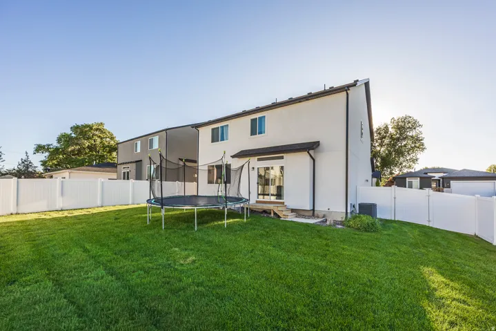 Expansive backyard with a manicured lawn, white privacy fencing, and a white stucco exterior