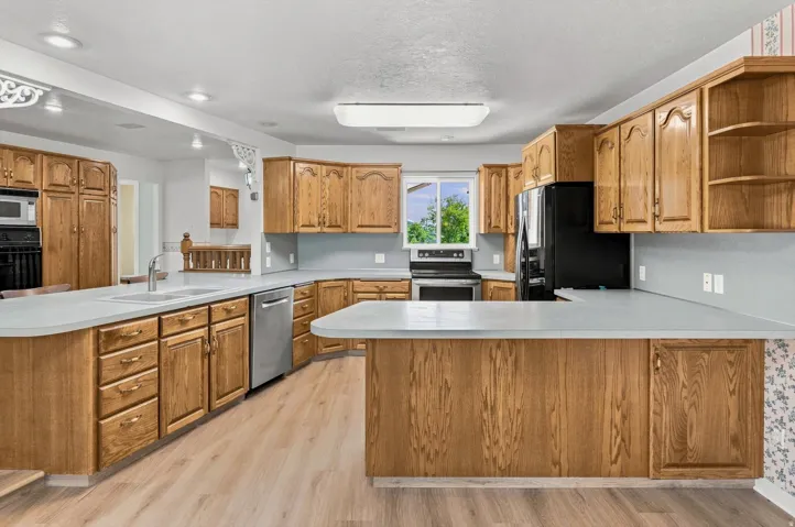 Expansive kitchen with wood cabinetry, light countertops, wood-finish flooring, and a stainless steel dishwasher