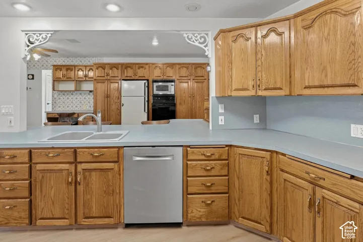 Kitchen featuring wood cabinetry, light-toned countertops, a stainless-steel dishwasher, and a double basin sink