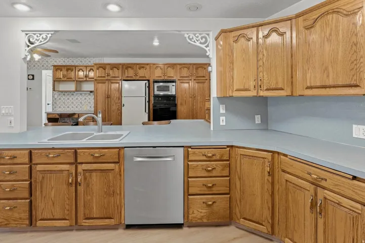 Kitchen featuring wood cabinetry, light-toned countertops, a stainless-steel dishwasher, and a double basin sink