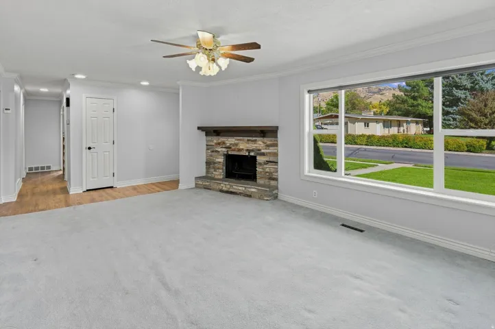 Spacious living area featuring a stone fireplace with a wood mantle, a large picture window, and recessed lighting