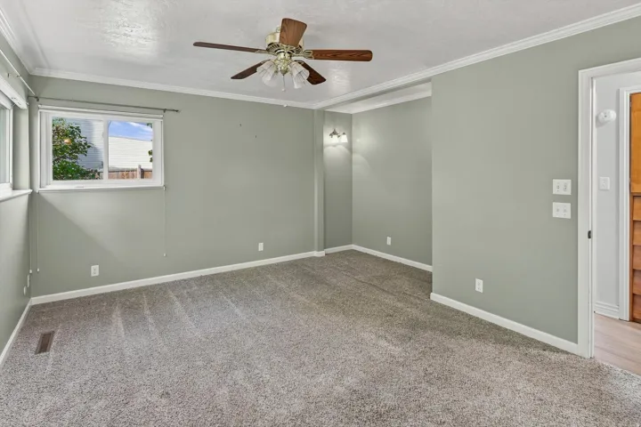 Neutral wall paint, ceiling fan, carpet flooring, crown molding, and wall sconces