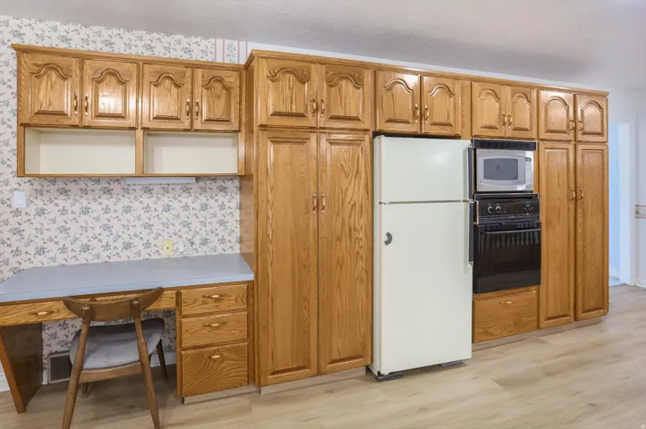 Wood-finish cabinetry, built-in desk with laminate countertop, integrated wall oven, and microwave