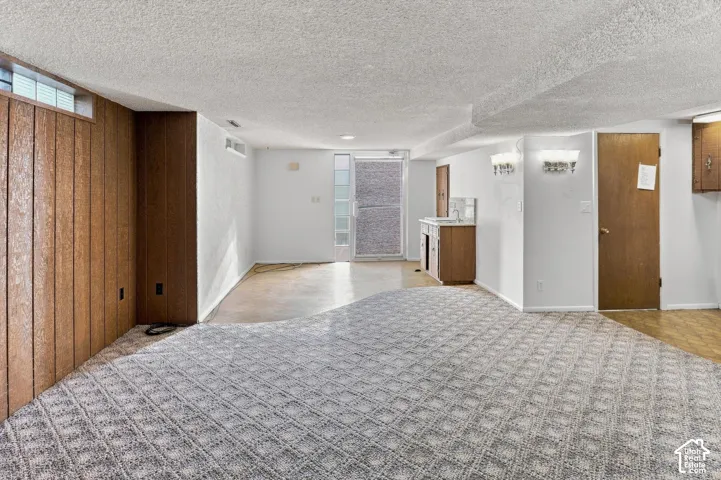 Basement living area featuring patterned carpet, wood paneling, a wet bar with a tile backsplash, and a glass-paneled door