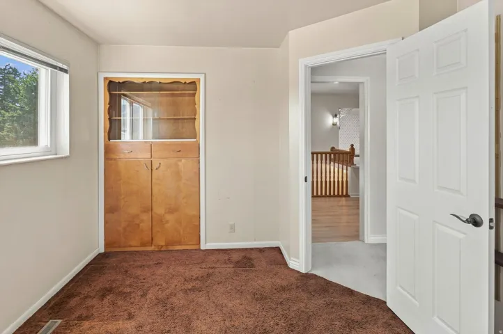 Built-in wood-finish cabinetry featuring glass display shelves, and a window with white trim