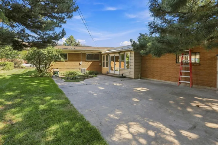 Expansive concrete patio with direct access to an enclosed sunroom featuring double glass doors and multiple windows