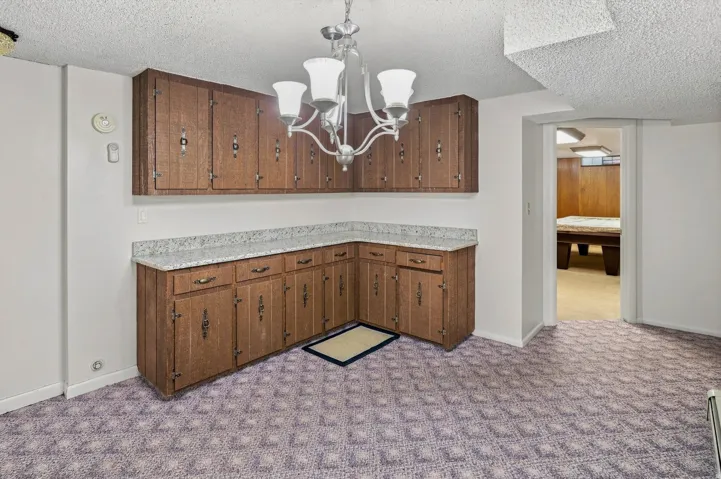 Wood-finish cabinetry with decorative hardware, light-toned countertops, and an overhead chandelier with four lights