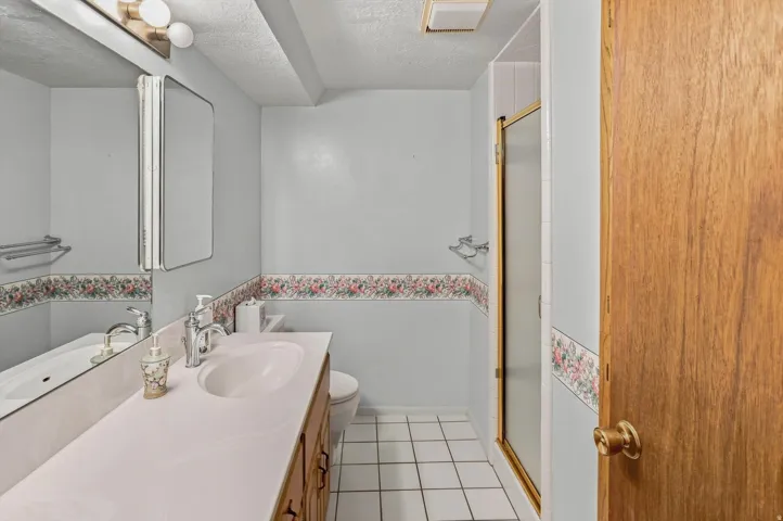 Vanity with integrated sink, wood-finish cabinetry, wall-mounted mirror, and tile flooring