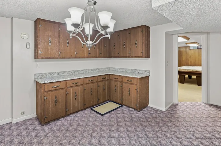Corner wood-finish cabinetry with granite-look countertops and an overhead chandelier