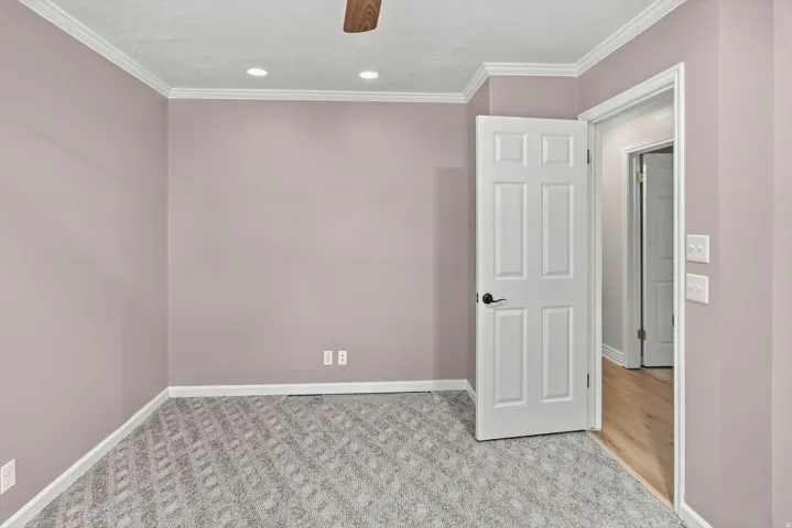 Recessed ceiling lights, crown molding, wood-finish ceiling fan, paneled interior door, and patterned carpet