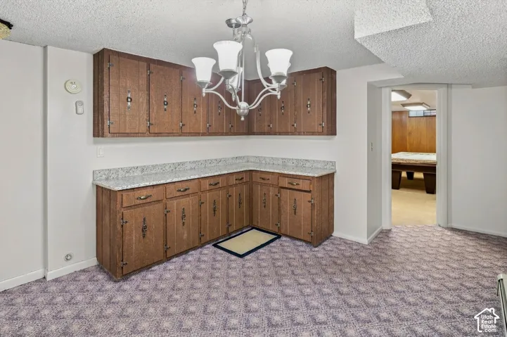 Wood-finish cabinetry with decorative hardware, light-toned countertops, and an overhead chandelier with four lights