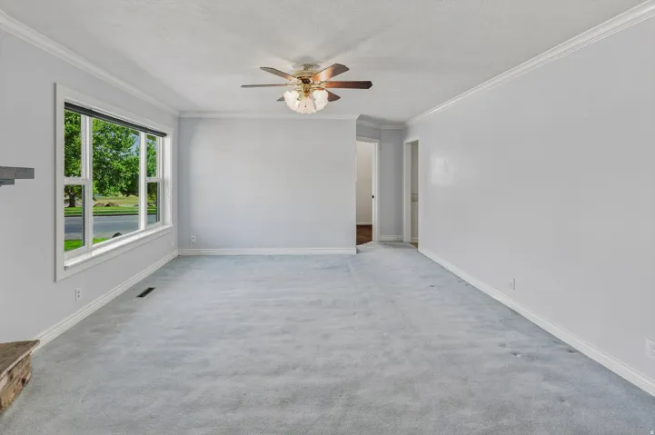Light-colored carpeting, white crown molding, and a ceiling fan with integrated lighting