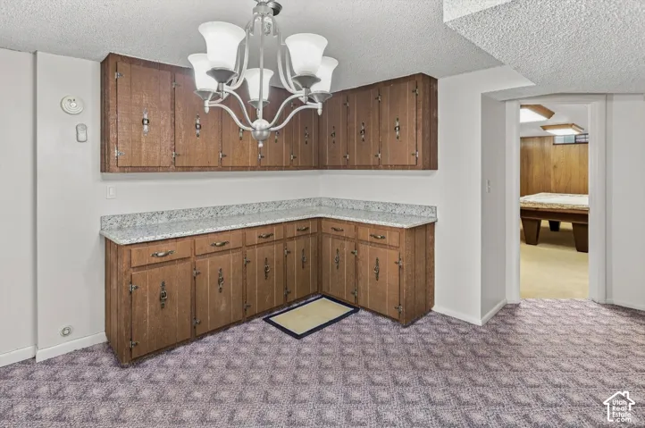 Corner wood-finish cabinetry with granite-look countertops and an overhead chandelier