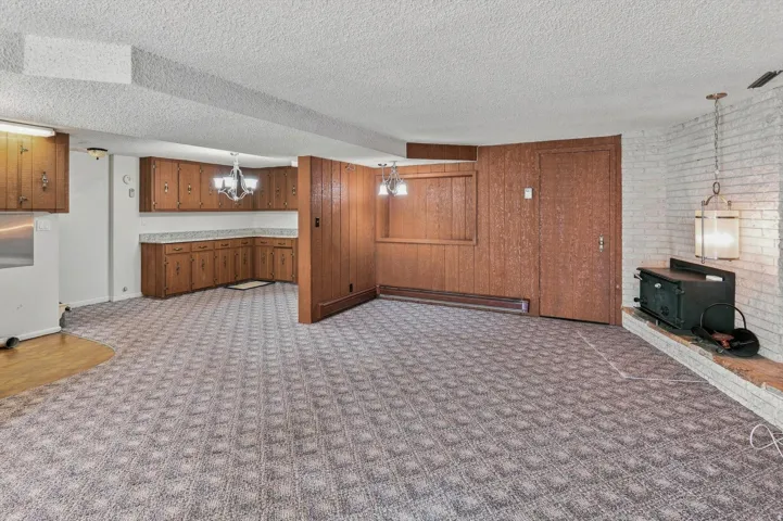 Spacious room featuring patterned carpet, wood-finish paneling, and a white brick fireplace with a hearth