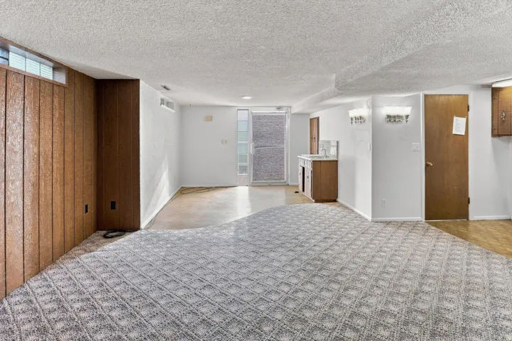 Basement living area featuring patterned carpet, wood paneling, a wet bar with a tile backsplash, and a glass-paneled door