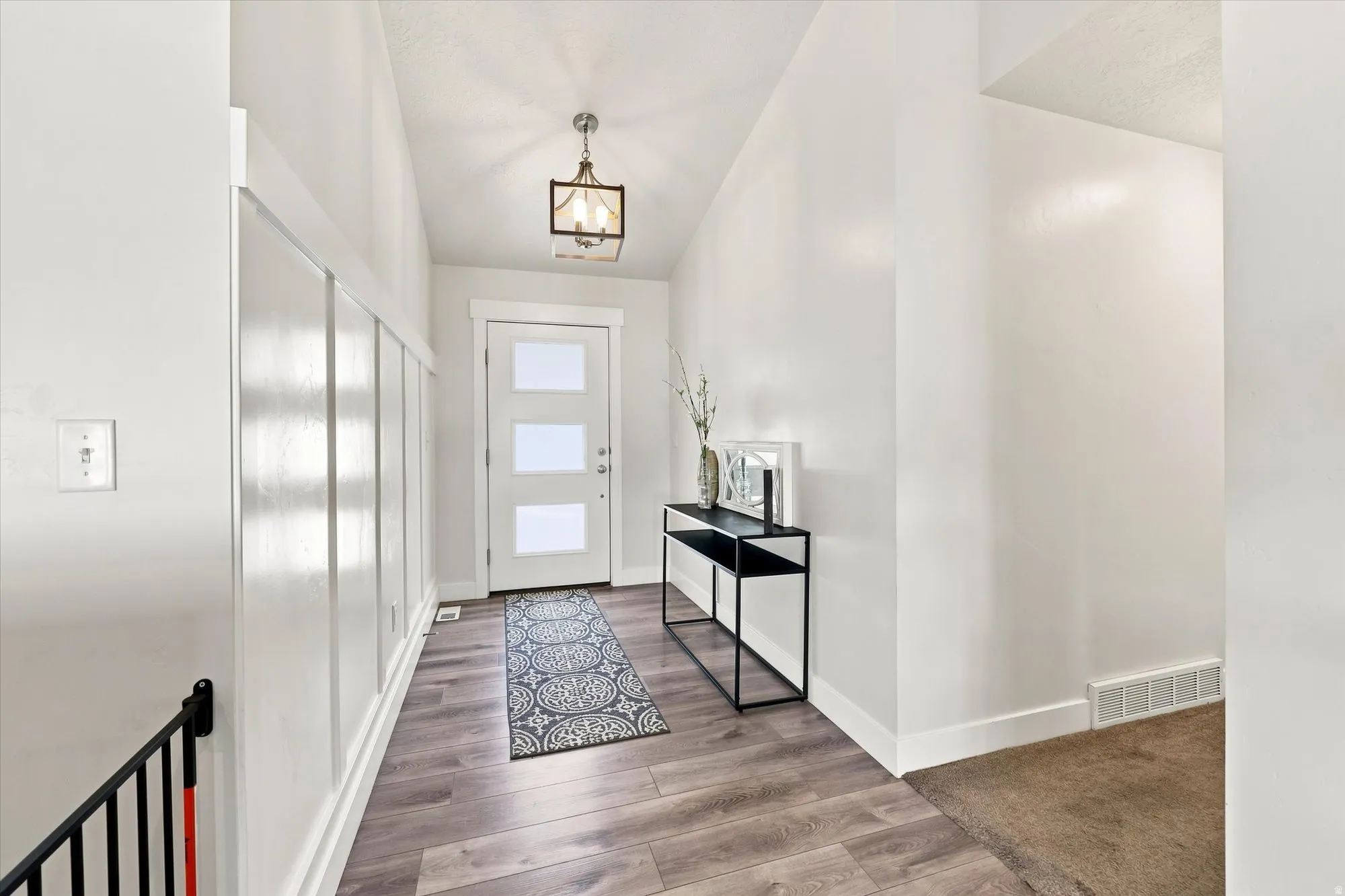Entryway featuring wood-finish flooring, white board and batten wall detailing, a contemporary pendant light fixture, and a white entry door with frosted glass panels
