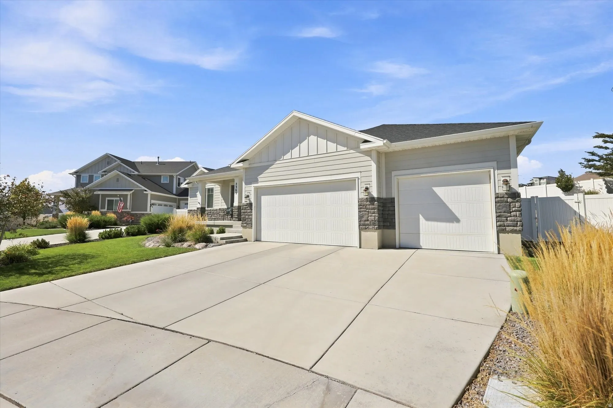 Contemporary exterior with light-toned siding, dark roof, two garage doors, stone accents, and a concrete driveway