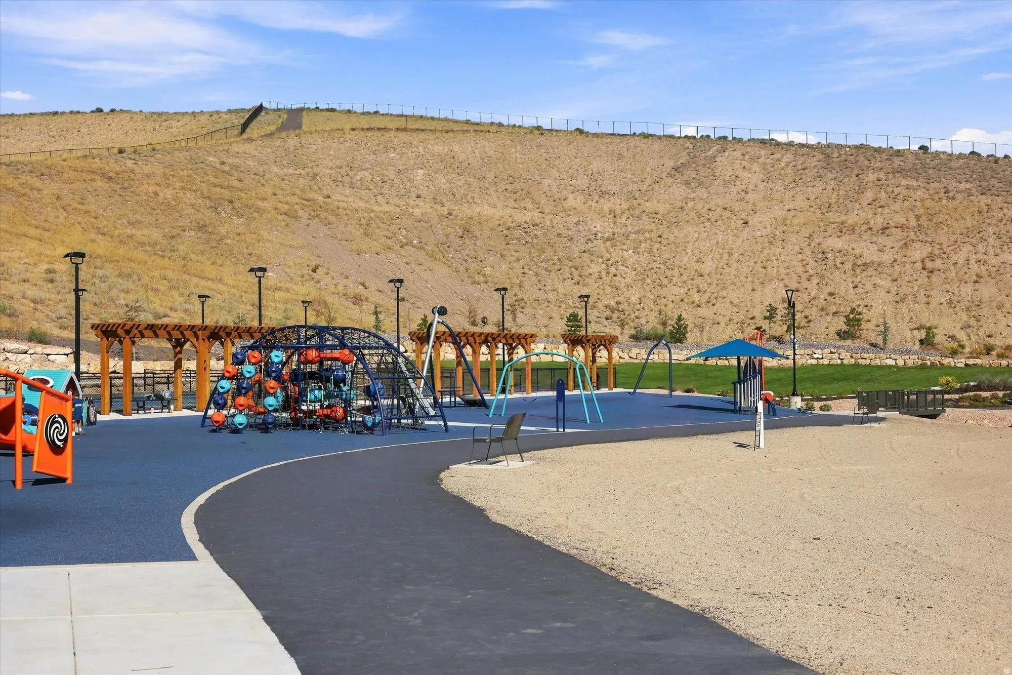 Playground area featuring rubberized surfacing, swings, and climbing structures under a blue canopy
