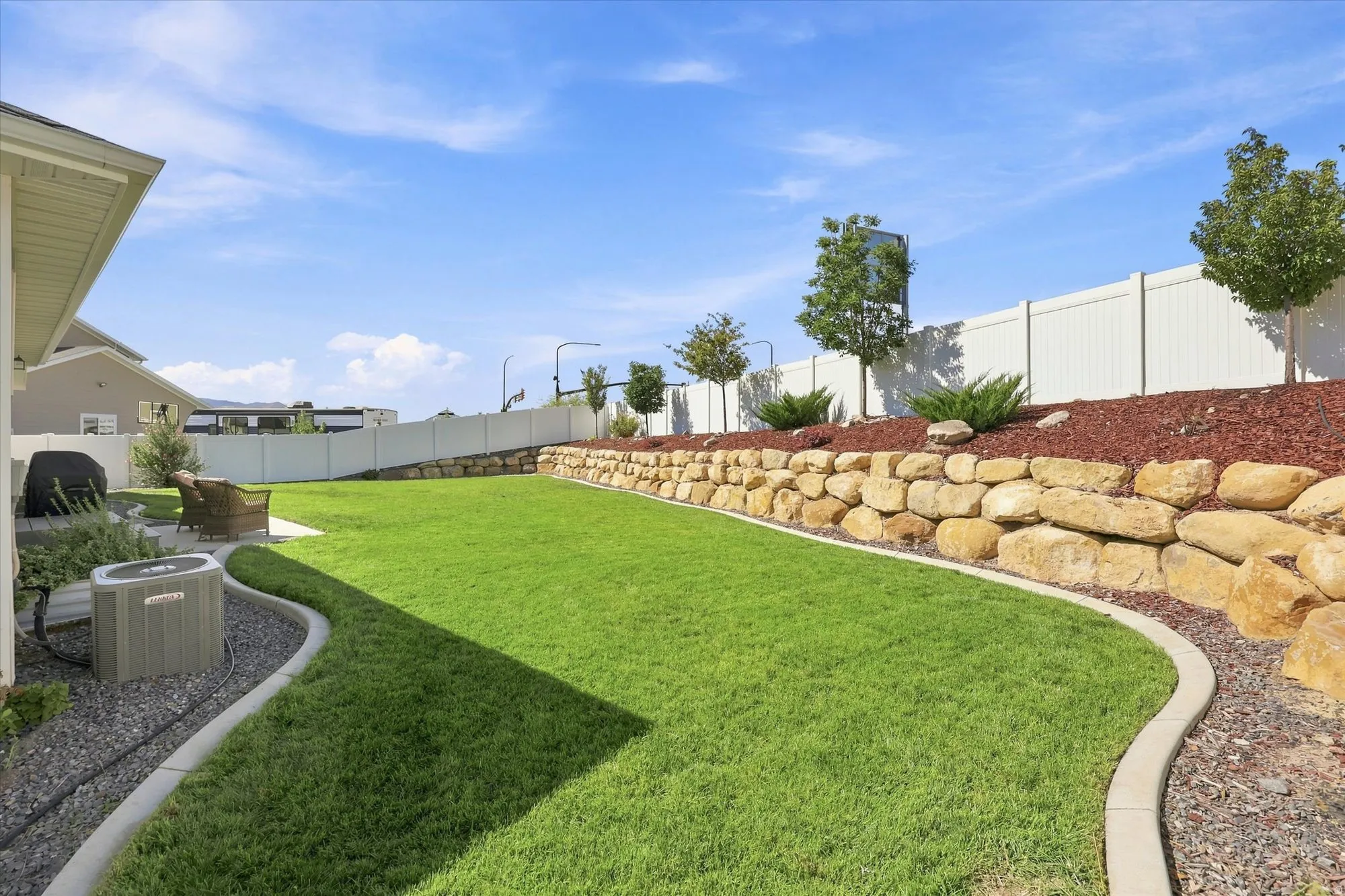 Expansive backyard with a manicured lawn, stone retaining wall, and defined landscaping beds