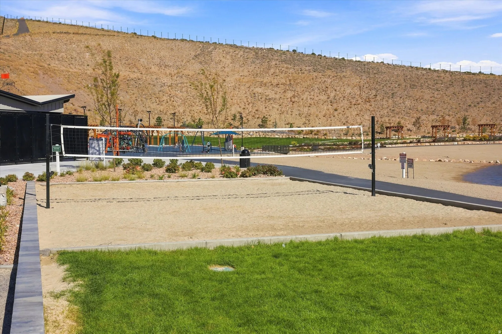 Sand volleyball court with a net, bordered by manicured landscaping and a paved pathway
