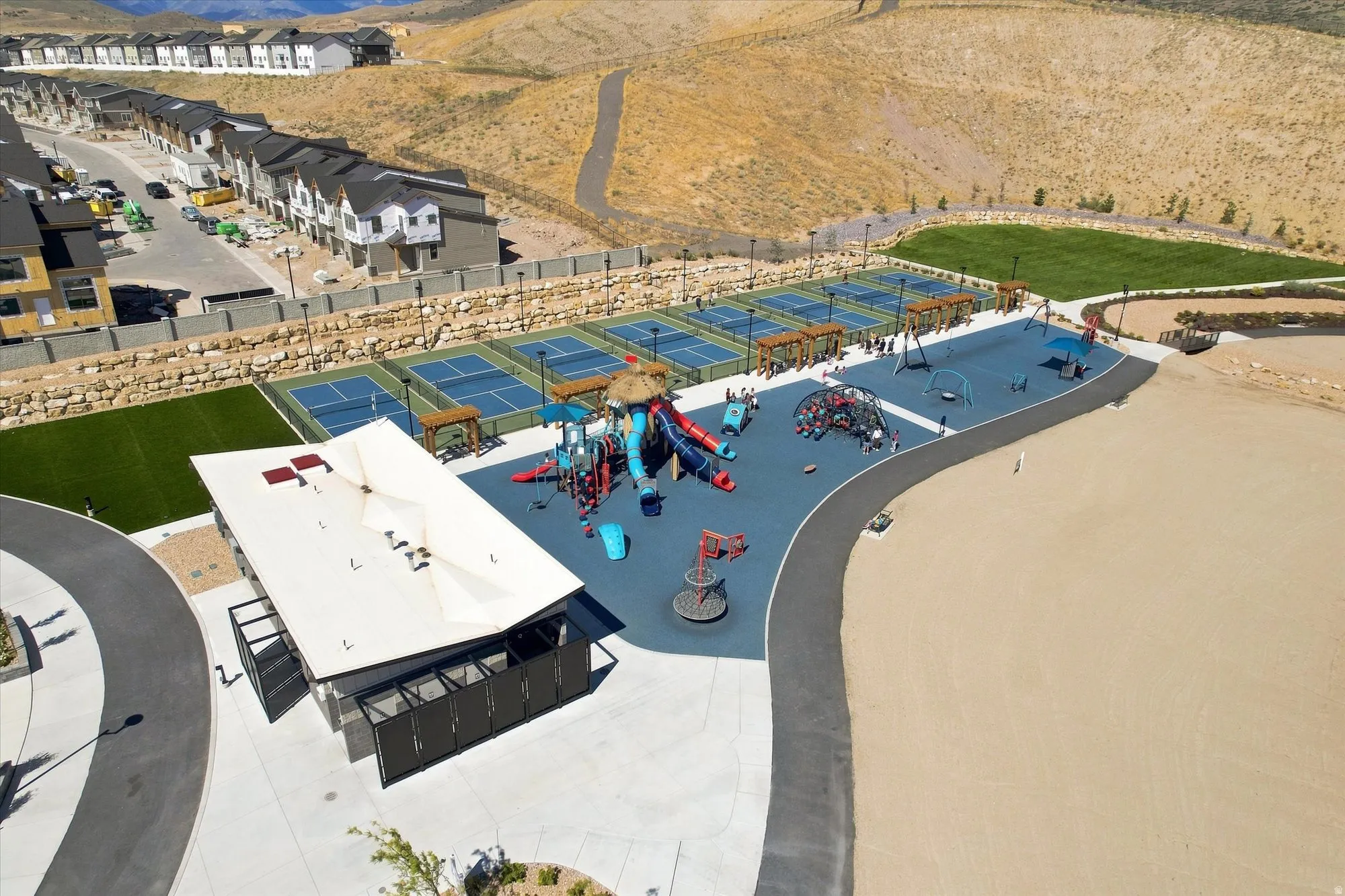 Community recreational area featuring multiple sports courts, a playground with various structures, a covered pavilion, and walking paths