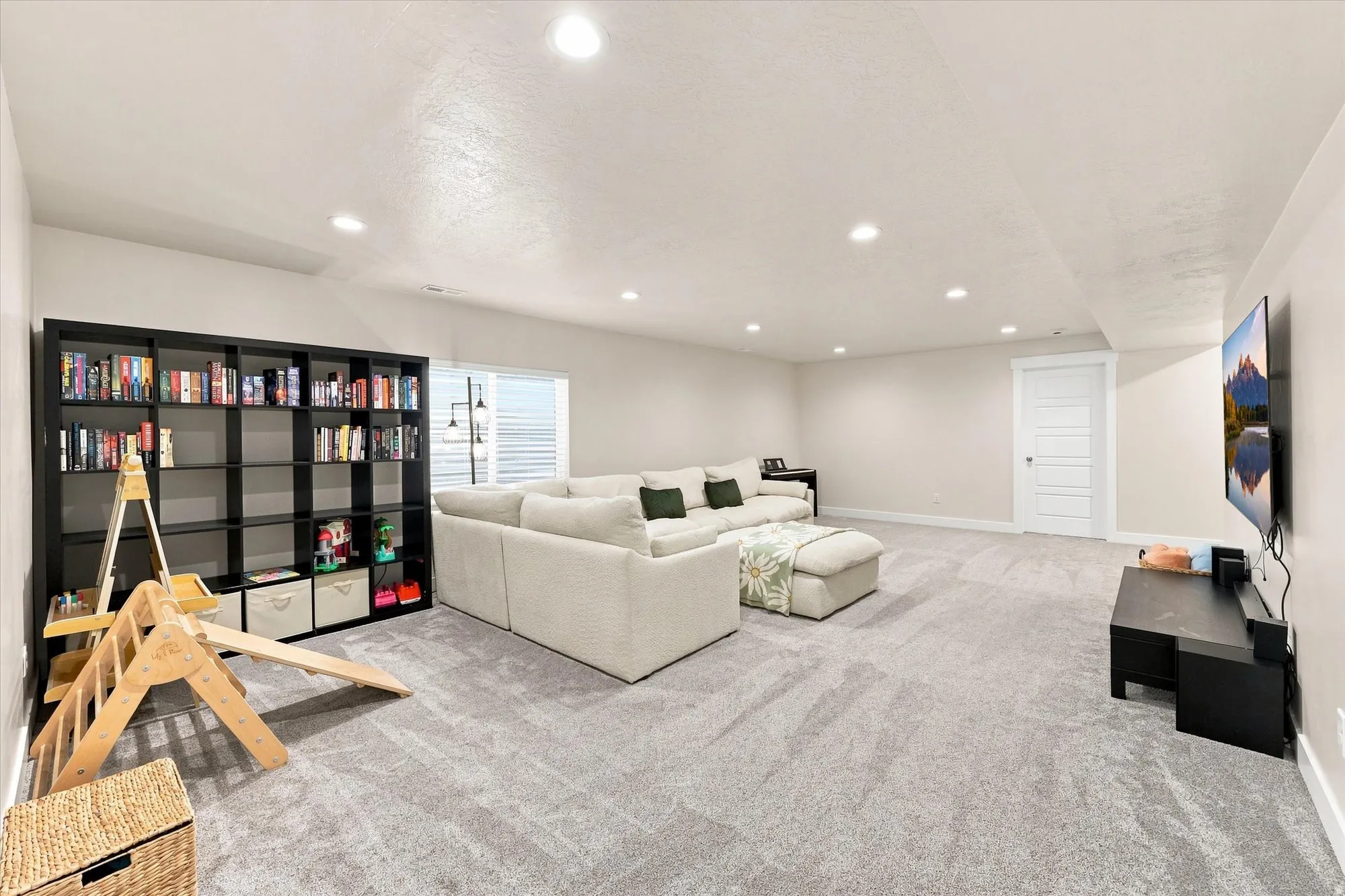 Recessed lighting illuminates a spacious room featuring light-toned carpeting and a built-in shelving unit