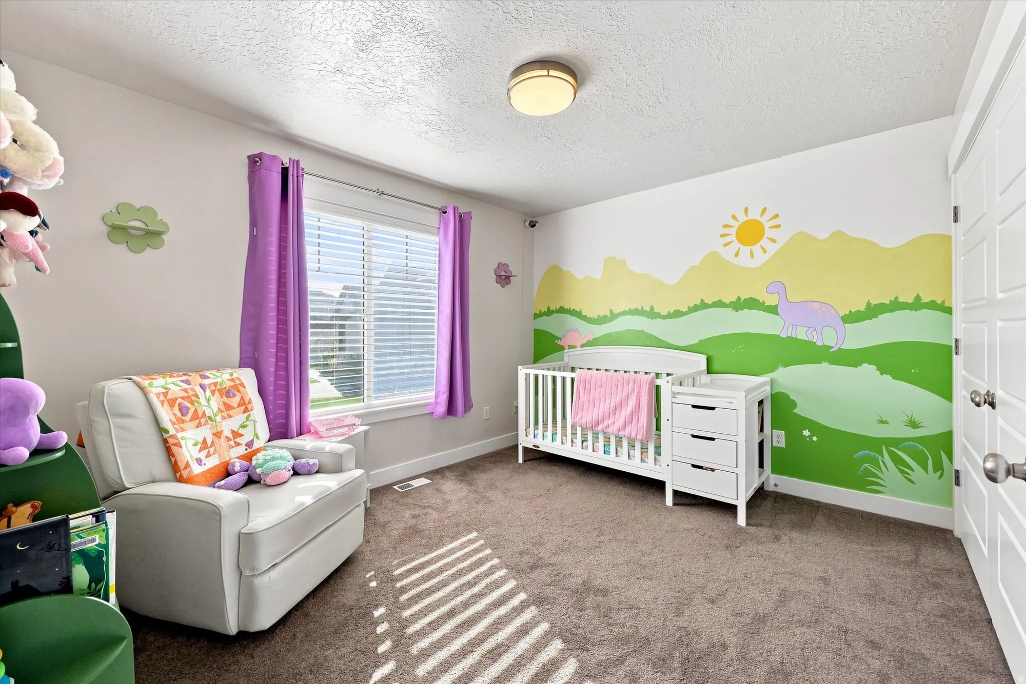 Wall-to-wall carpeting, window with blinds and purple curtains, flush mount ceiling light, white paneled door, and a decorative wall mural