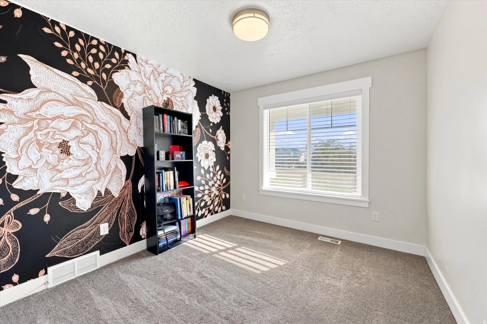 Accent wall with floral pattern, neutral carpet flooring, recessed window with blinds, ceiling-mounted light fixture, and light-colored walls