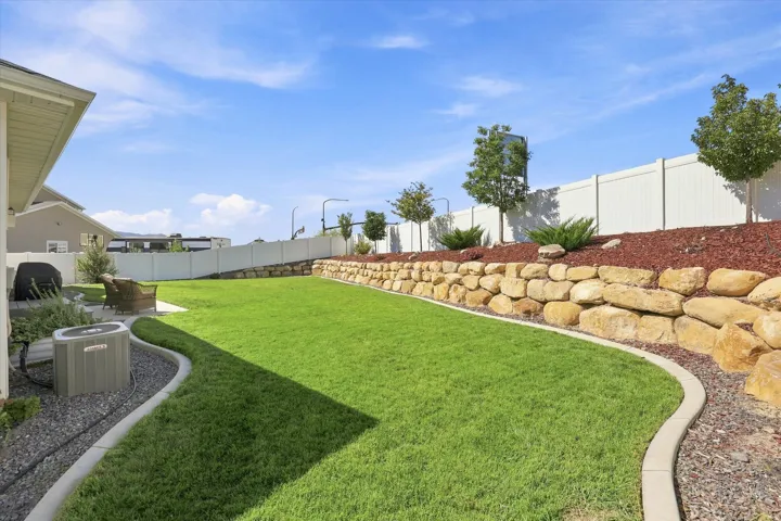 Expansive backyard with a manicured lawn, stone retaining wall, and defined landscaping beds