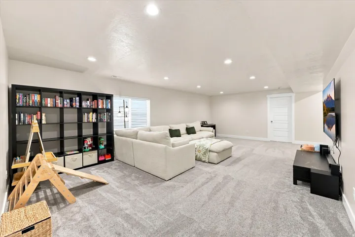 Recessed lighting illuminates a spacious room featuring light-toned carpeting and a built-in shelving unit