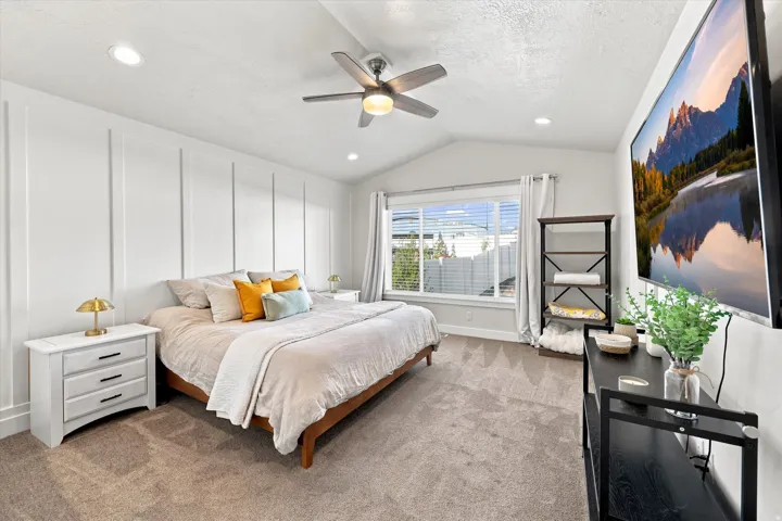 Vaulted ceiling with a ceiling fan, recessed lighting, accent wall with vertical paneling, and a large window with blinds