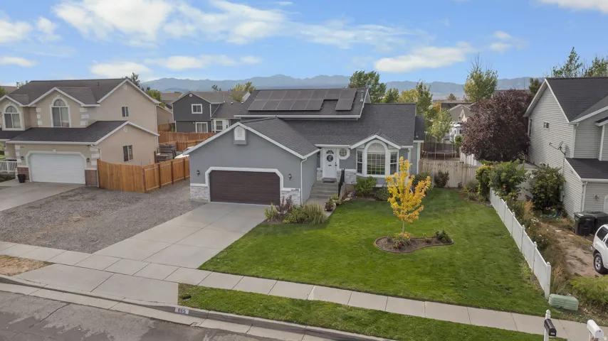 Ranch-style residence featuring a gray exterior, bay window, front-facing garage with a dark wood-finish door, solar panels, and a concrete driveway