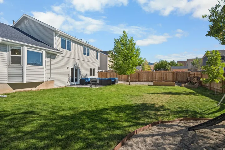 Expansive backyard featuring a lush lawn, privacy fencing, mature trees, and a paved patio area with direct access to the interior