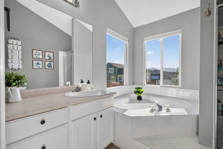 Vaulted ceiling bathroom featuring a built-in corner soaking tub, double windows, white vanity cabinetry with a single sink, and a built-in shower enclosure