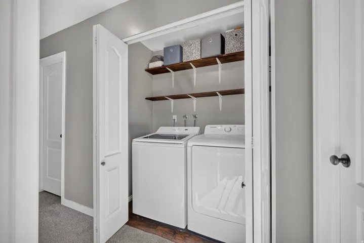 Laundry closet featuring built-in wood-finish shelving and a wood-finish floor