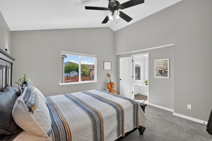 Vaulted ceiling with a ceiling fan, light gray wall finish, carpeted flooring, and a window with a white frame