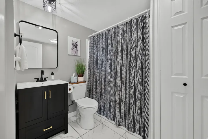 Bathroom featuring a black vanity with gold-tone hardware, a white integrated sink, a matte black faucet, and white tile flooring