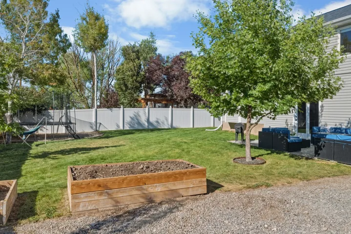 Expansive lawn area with a white privacy fence, mature trees, a gravel pathway, and a patio with outdoor seating