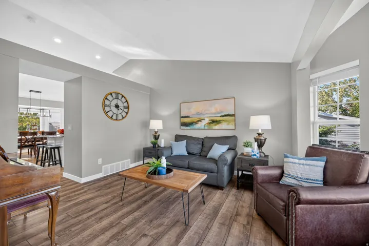 Vaulted ceiling with recessed lighting, wood-finish flooring, and a large window with blinds