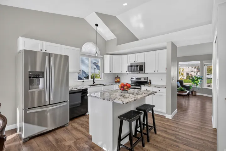 Kitchen featuring white cabinetry, stainless steel appliances, a center island with a stone countertop, wood-finish flooring, and a vaulted ceiling
