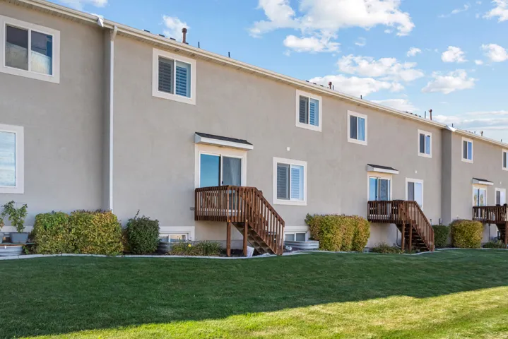 Stucco exterior featuring multiple windows with trim, sliding glass door access to a wood deck, and a manicured lawn