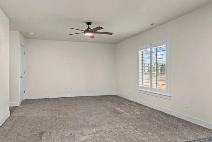Neutral-toned wall paint, plantation shutters, grey carpeting, ceiling fan with integrated lighting, and a white interior door