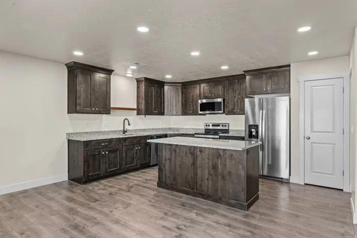 Kitchen featuring wood-finish flooring, dark wood cabinetry, light-toned countertops, and stainless steel appliances