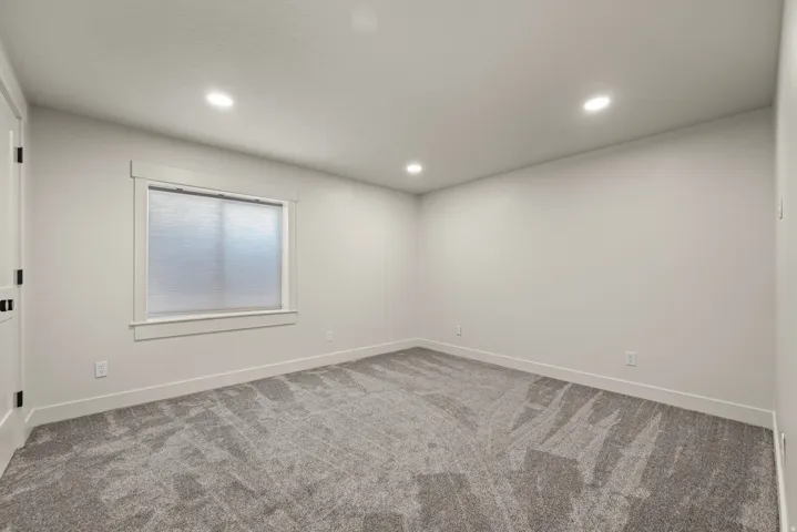 Neutral wall paint, recessed ceiling lighting, light gray carpet flooring, and a single window with blinds