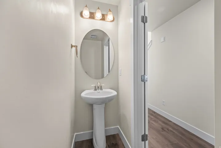 Pedestal sink with chrome fixtures, oval mirror, and a three-light vanity fixture